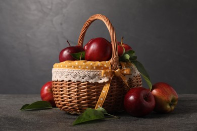 Photo of Ripe red apples and leaves in wicker basket on dark grey table