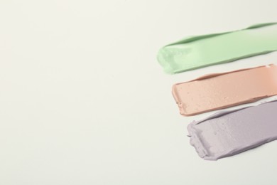 Strokes of pink, green and purple color correcting concealers on white background