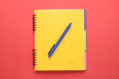 Photo of Yellow notebook and pen on red background, top view