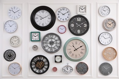 Photo of Collection of different clocks hanging on white wall