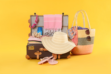 Photo of Bag and open vintage suitcase with different beach objects packed for summer vacation on orange background