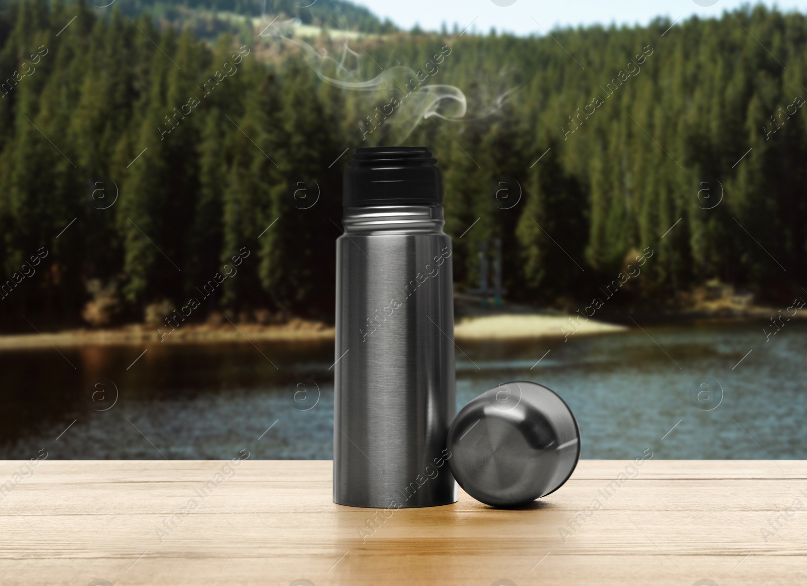 Image of Thermos on wooden table against blurred mountain landscape