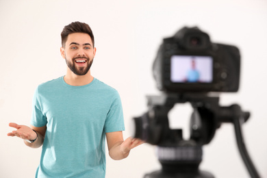 Young blogger recording video on camera against white background