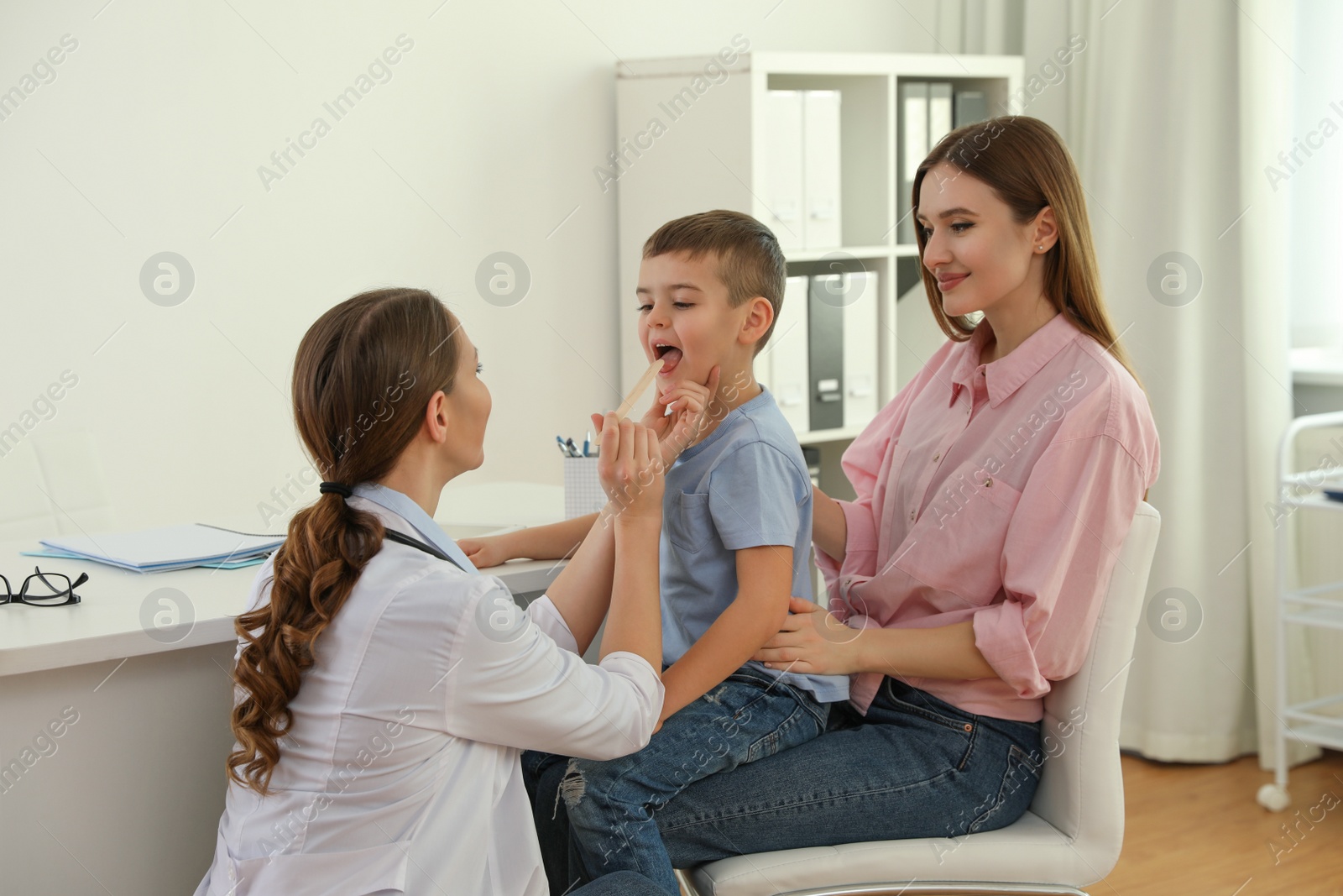 Photo of Mother and son visiting pediatrician. Doctor examining little patient's throat in hospital