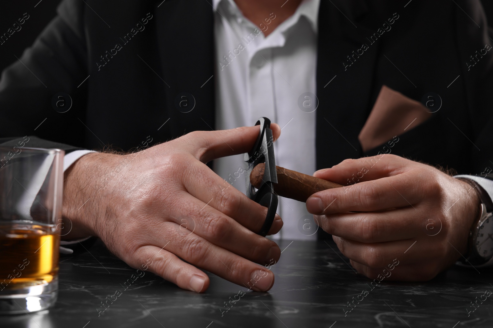 Photo of Man cutting tip of cigar at dark marble table, closeup