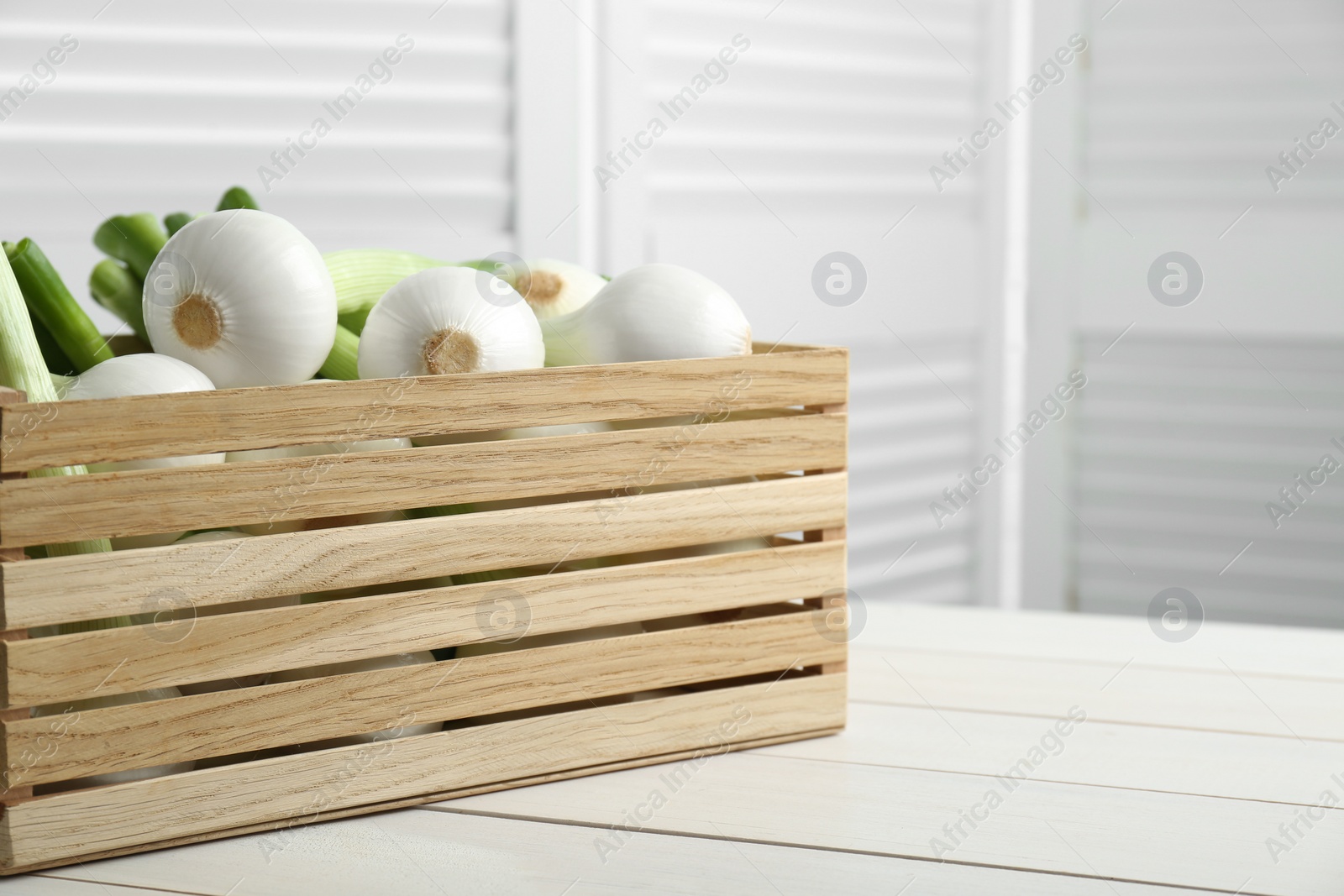 Photo of Crate with green spring onions on white wooden table, closeup. Space for text