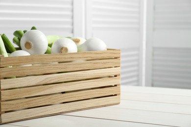 Photo of Crate with green spring onions on white wooden table, closeup. Space for text