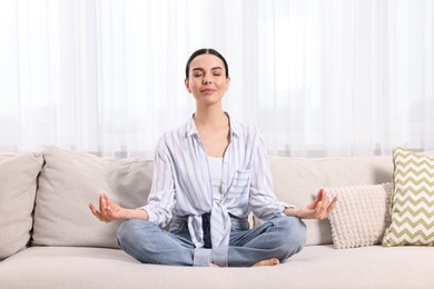Woman meditating on sofa at home. Harmony and zen