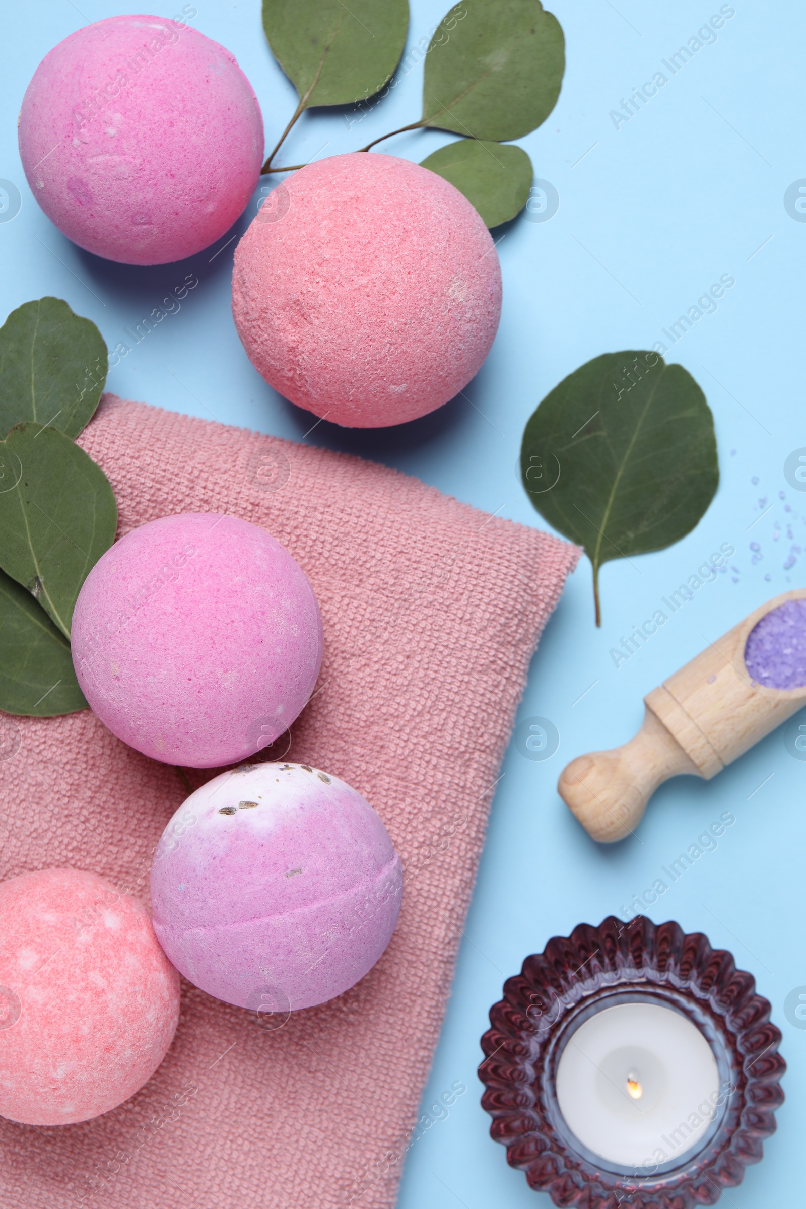 Photo of Bath bombs, eucalyptus leaves, burning candle and sea salt on light blue background, flat lay