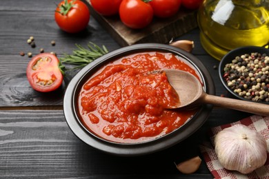 Photo of Homemade tomato sauce in bowl, spoon and fresh ingredients on black wooden table