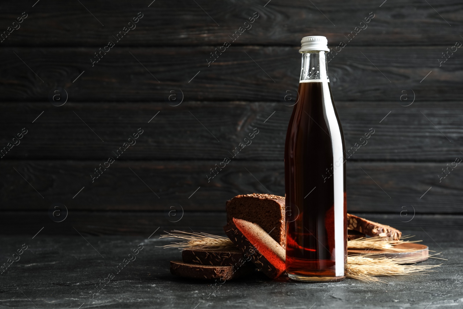 Photo of Bottle of delicious fresh kvass, spikelets and bread on grey table. Space for text