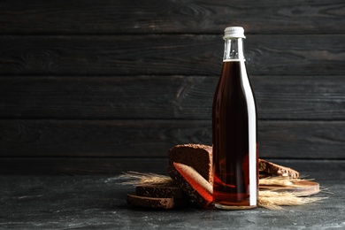 Photo of Bottle of delicious fresh kvass, spikelets and bread on grey table. Space for text