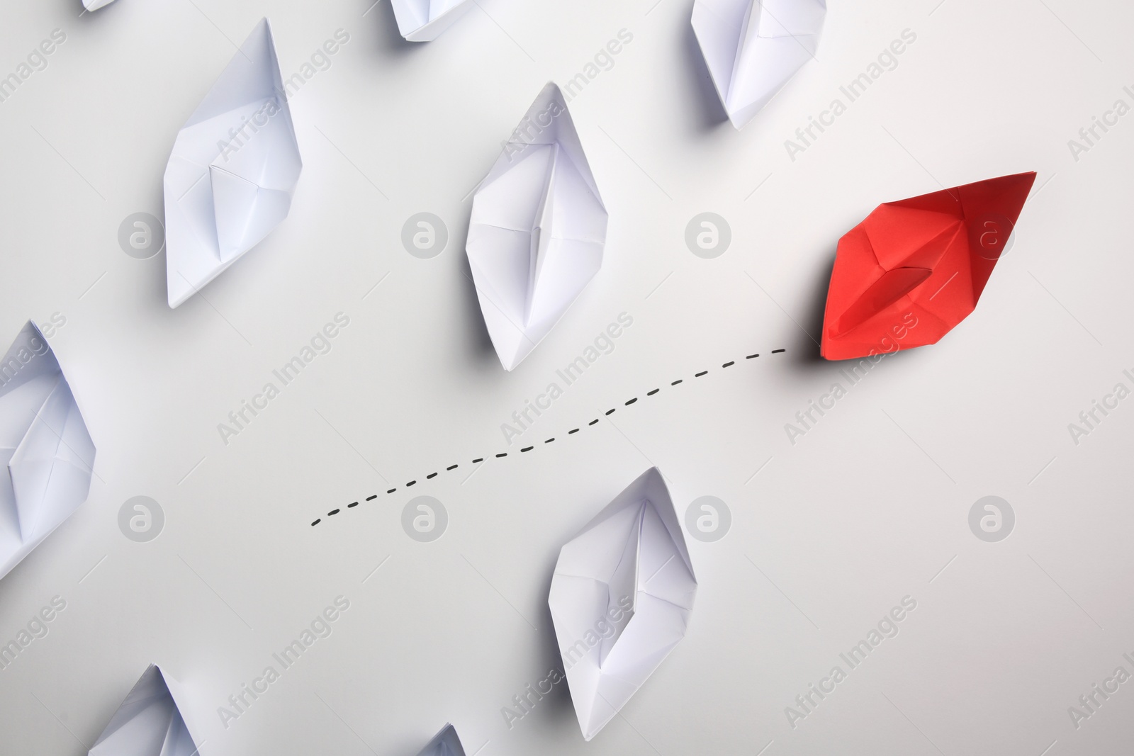 Photo of Red paper boat floating away from others on white background, flat lay. Uniqueness concept