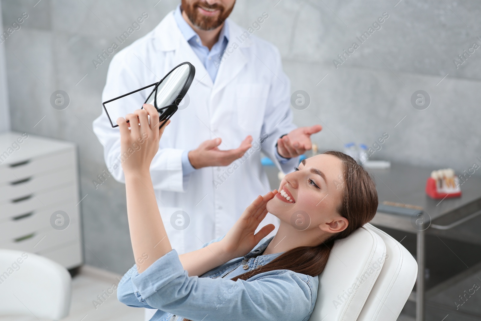 Photo of Young woman looking at her new dental implants in mirror indoors