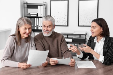 Photo of Elderly couple consulting insurance agent about pension plan at wooden table indoors