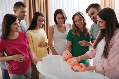 Pregnant women with men learning how to bathe baby at courses for expectant parents indoors