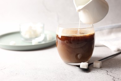 Pouring milk into cup with coffee on white textured table, closeup