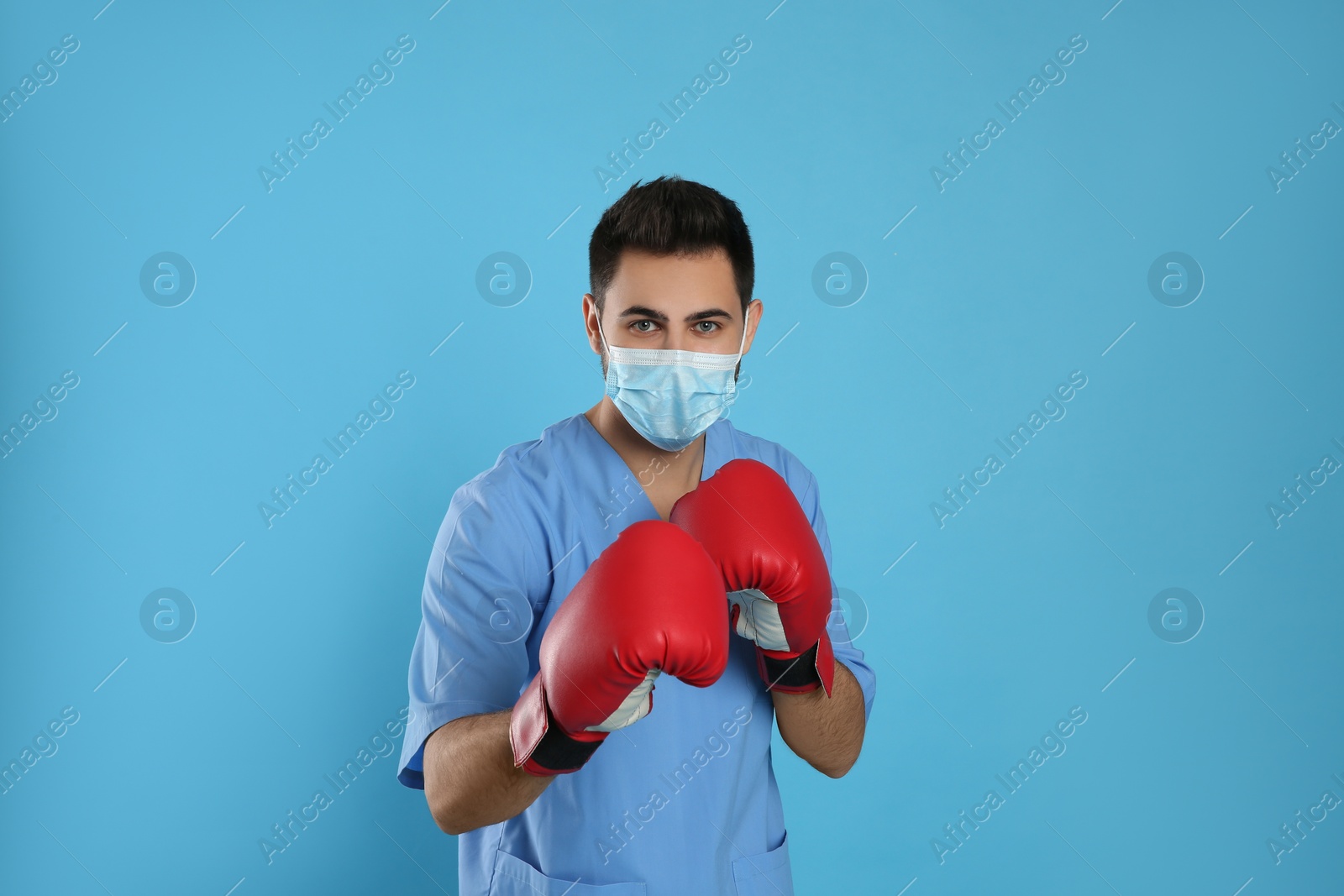 Photo of Doctor with protective mask and boxing gloves on light blue background. Strong immunity concept