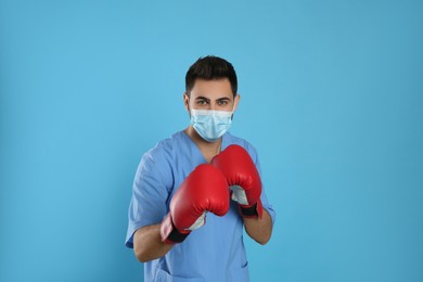 Photo of Doctor with protective mask and boxing gloves on light blue background. Strong immunity concept