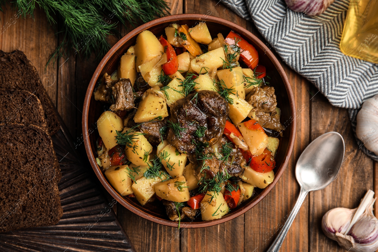 Photo of Tasty cooked dish with potatoes in earthenware served on wooden table, flat lay