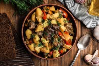 Photo of Tasty cooked dish with potatoes in earthenware served on wooden table, flat lay