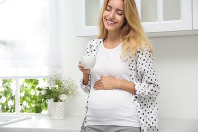 Photo of Beautiful pregnant woman drinking tea in kitchen