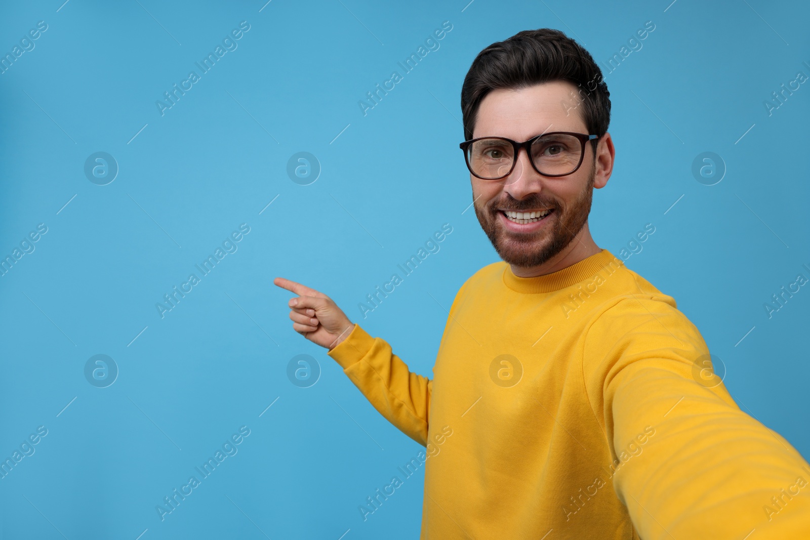 Photo of Smiling man taking selfie on light blue background, space for text