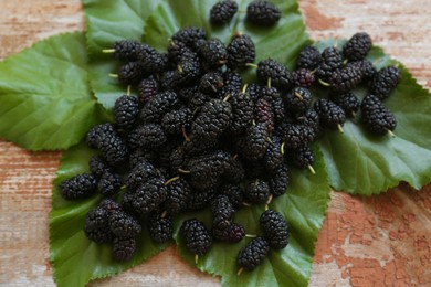 Heap of delicious ripe black mulberries and green leaves on wooden table, flat lay