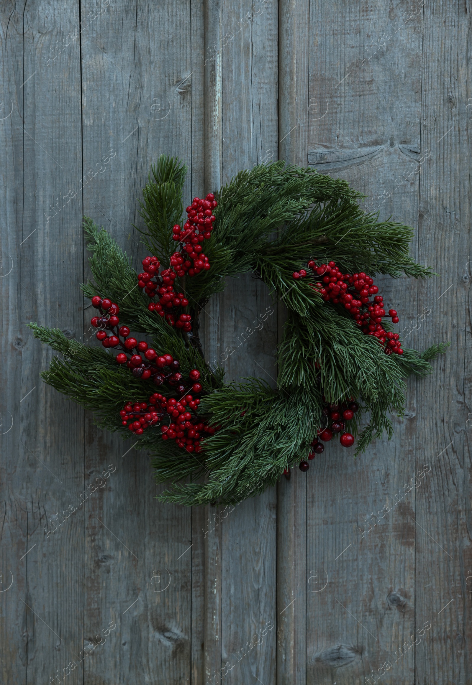 Photo of Beautiful Christmas wreath with red berries hanging on wooden wall