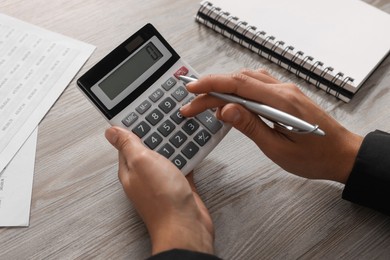 Photo of Woman using calculator at light wooden table, closeup