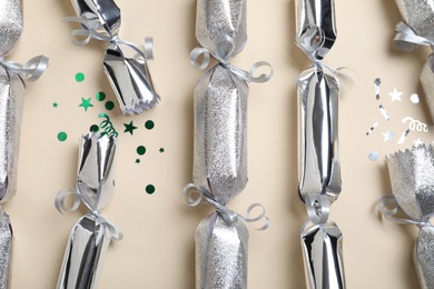 Open and closed silver Christmas crackers with shiny confetti on beige background, flat lay