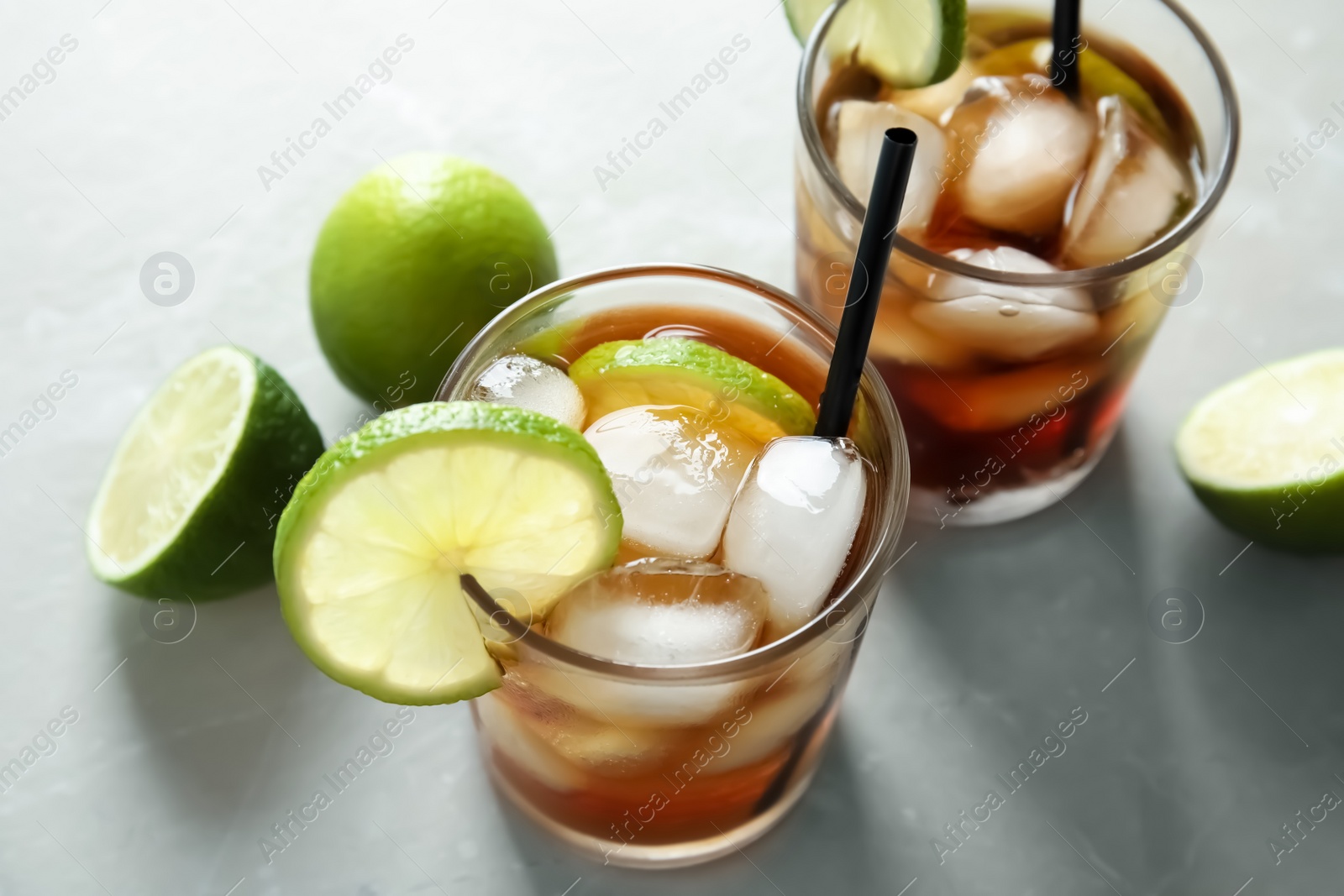 Photo of Glasses of cocktail with cola, ice and cut lime on light background