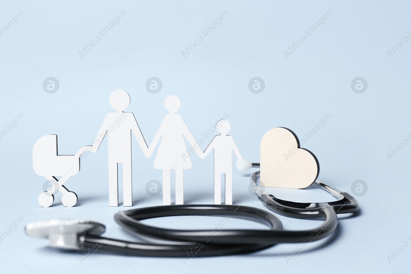 Photo of Figures of family stainding near stethoscope on light blue background. Space for text. Insurance concept