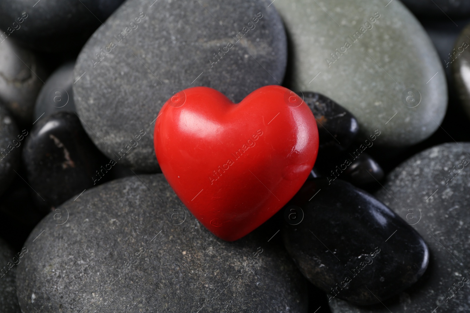 Photo of Red decorative heart on pebble stones, closeup