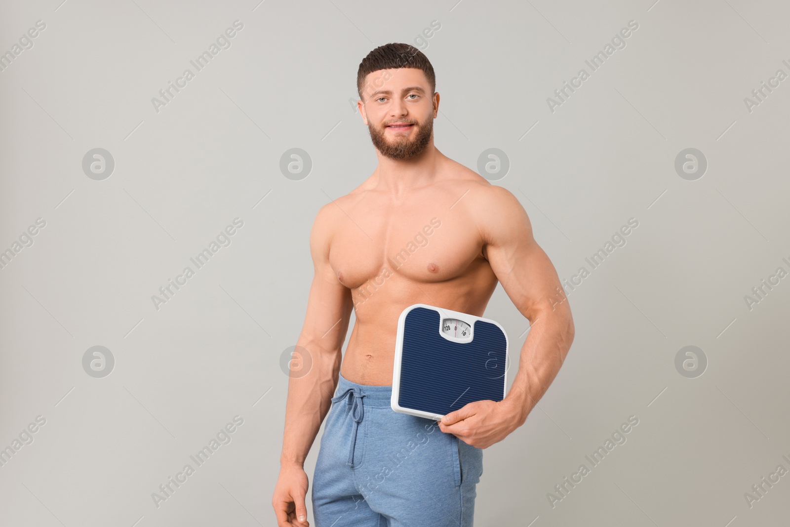 Photo of Happy athletic man holding scales on light grey background. Weight loss concept