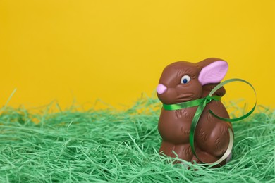 Photo of Easter celebration. Cute chocolate bunny on grass against yellow background, space for text