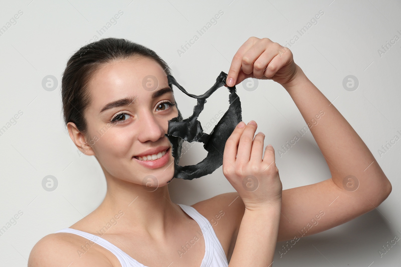 Photo of Beautiful young woman removing black mask from her face on white background