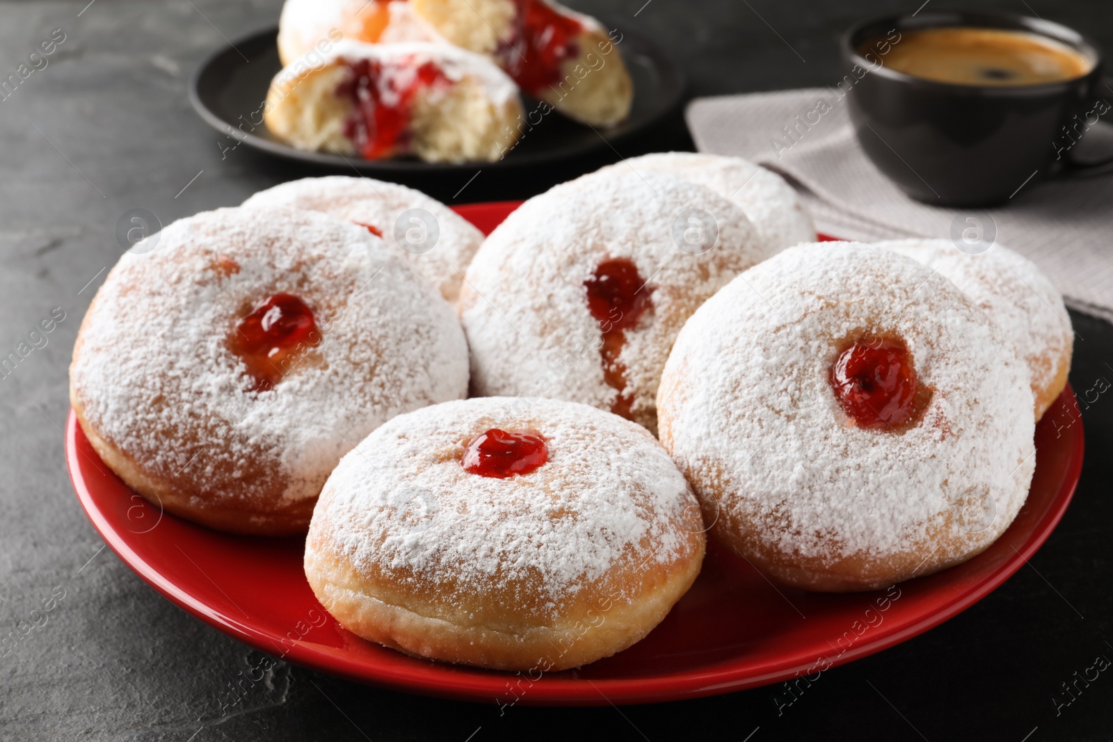 Photo of Delicious donuts with jelly and powdered sugar on black table, closeup