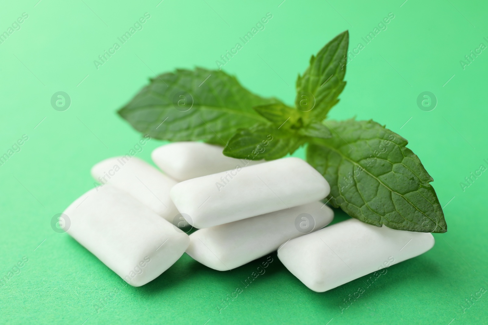 Photo of Tasty white chewing gums and mint leaves on green background, closeup