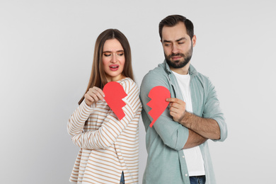 Couple with torn paper heart on light background. Relationship problems