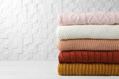 Photo of Stack of warm clothes on white wooden table against textured wall, space for text. Autumn season