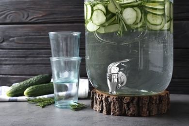 Photo of Composition with jar dispenser of fresh cucumber water on table against dark background