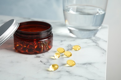 Photo of Jar with cod liver oil pills and glass of water on table