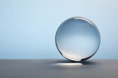 Transparent glass ball on table against light blue background. Space for text