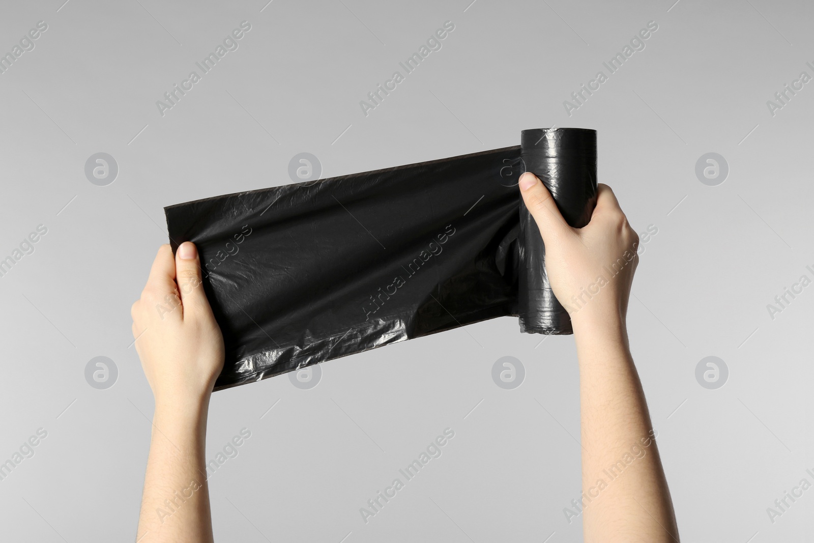 Photo of Woman holding roll of black garbage bags on light grey background, closeup