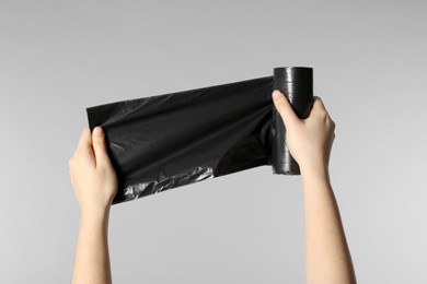 Photo of Woman holding roll of black garbage bags on light grey background, closeup