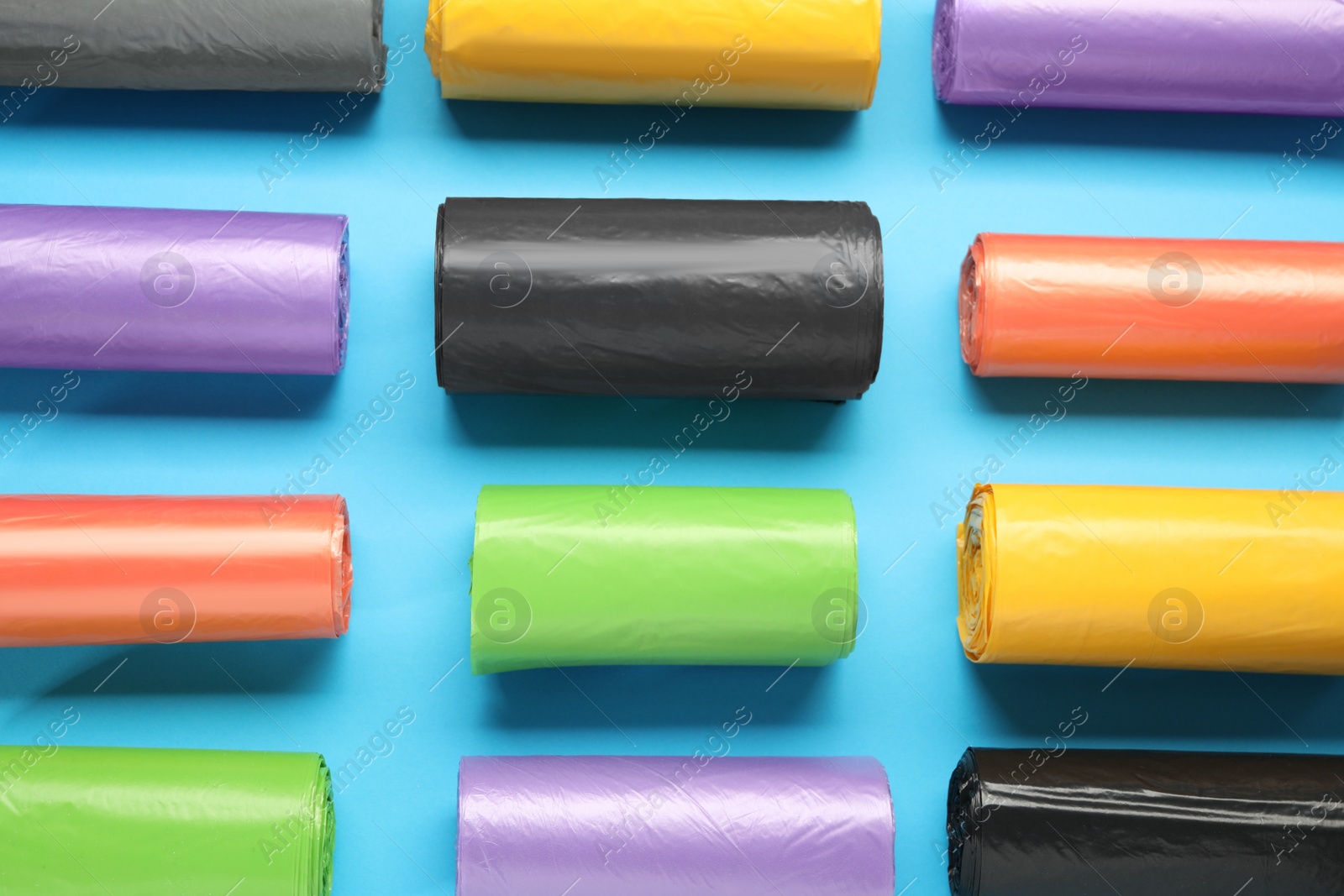 Photo of Rolls of different garbage bags on light blue background, flat lay