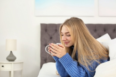 Beautiful young woman lying with cup in bed at home. Winter atmosphere