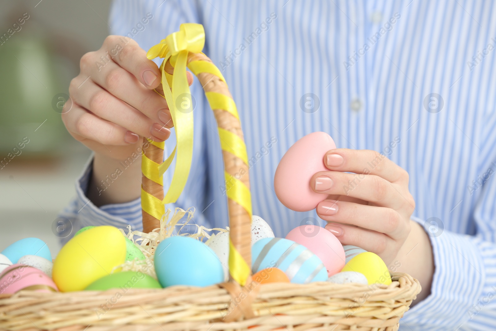 Photo of Woman putting painted egg into Easter basket, closeup