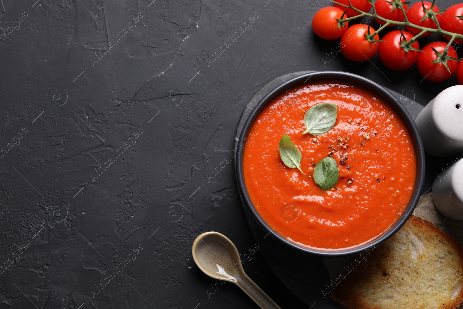 Photo of Delicious tomato cream soup served on black textured table, flat lay. Space for text